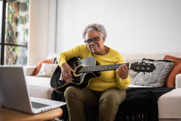 donna anziana che impara a suonare la chitarra in una lezione online a casa - plucking an instrument foto e immagini stock