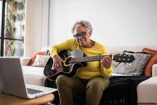 Senior woman learning to play guitar at an online class at home