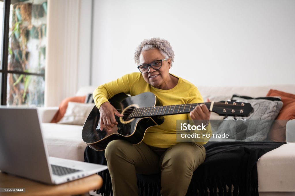 Senior woman learning to play guitar at an online class at home Playing Stock Photo
