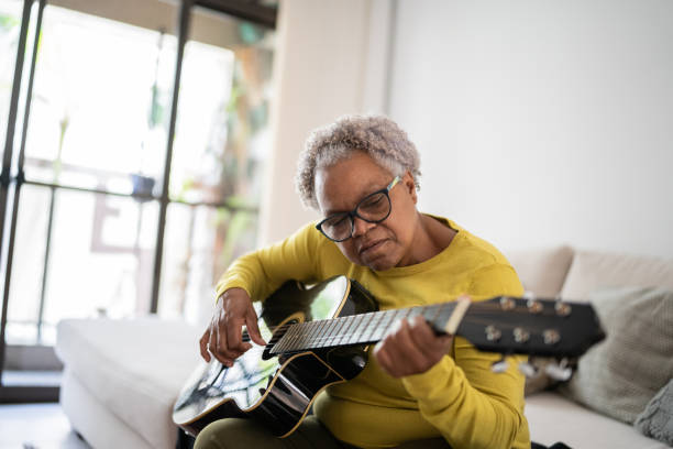 istock Senior woman playing guitar at home 1356377473