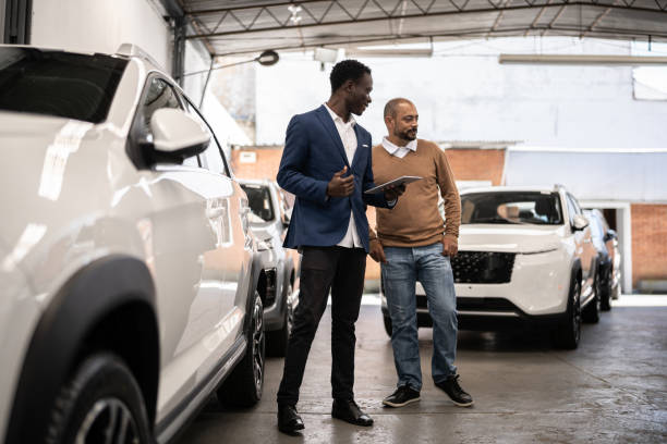 verkäufer zeigt dem kunden das auto in einem autohaus - retail shopping talking customer stock-fotos und bilder