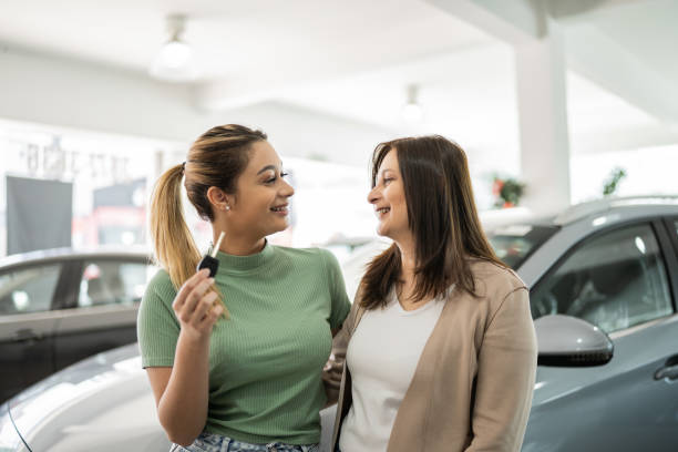 szczęśliwa dziewczyna teenger z matką pokazująca kluczyki do nowego samochodu w salonie samochodowym - car car rental car dealership key zdjęcia i obrazy z banku zdjęć