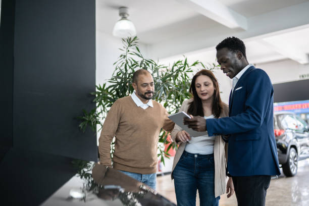 istock Car salesman using digital tablet talking about new car to customers in a store 1356380241