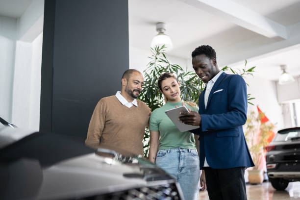 car salesman using digital tablet talking about new car to customers in a store - sales clerk imagens e fotografias de stock