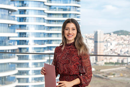 Beautiful businesswoman holding file in front of skyscrapers.
