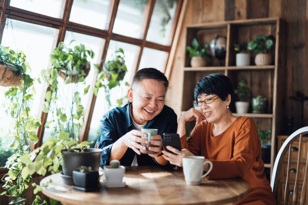 Happy senior Asian couple video chatting, staying in touch with their family using smartphone together at home. Senior lifestyle. Elderly and technology stock photo