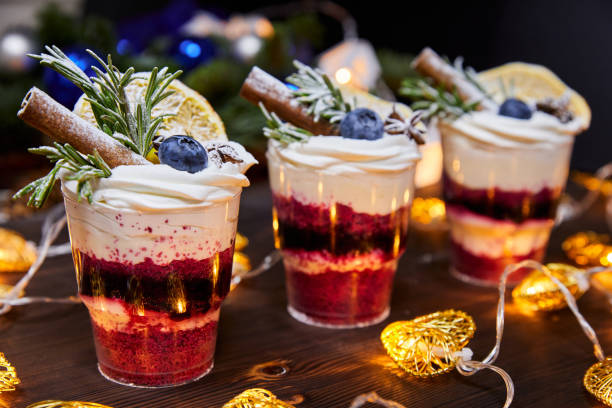 Christmas trifles in cups as a dessert, decorated with fresh blueberries and a vanilla stick, for a festive table on a background of glowing garlands Christmas trifles in cups as a dessert, decorated with fresh blueberries and a vanilla stick, for a festive table on a background of glowing garlands trifle stock pictures, royalty-free photos & images