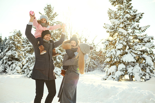 Young parents with children spending time in beautiful snowy woods standing in bright sunlight