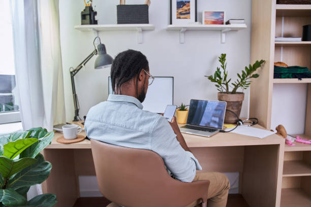istock Man wearing glasses looking at the smartphone while working with laptop at the table 1356383877
