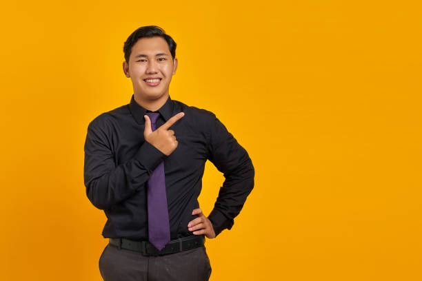 istock Smiling young Asian man pointing fingers at copy space on yellow background 1356384059