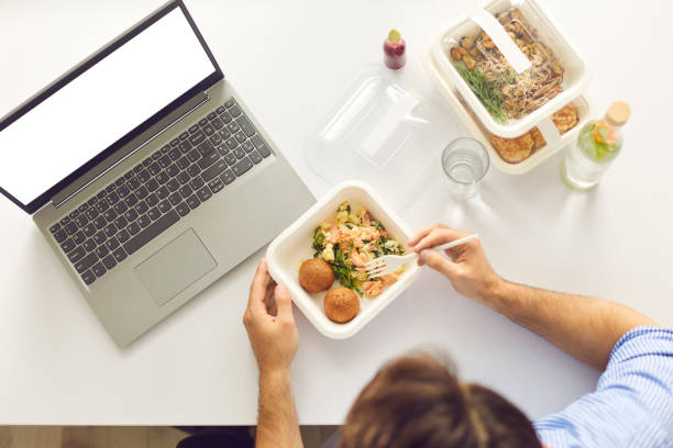 istock Busy man having lunch break at office desk with laptop computer with blank copy space screen 1356384297