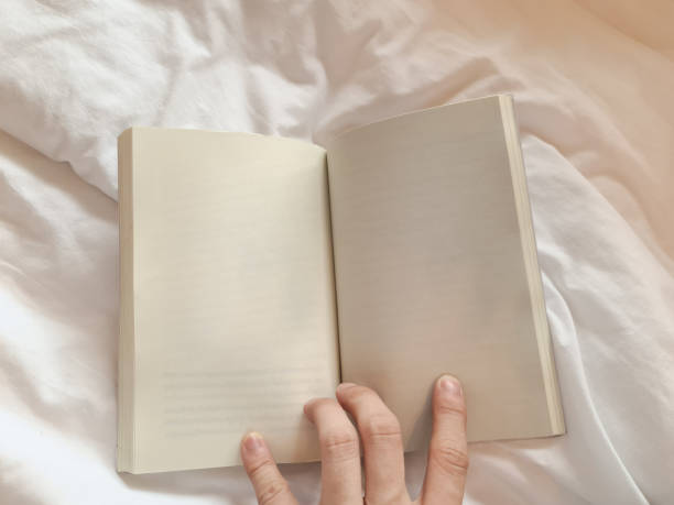 istock Hand holding blank page of a book on the bed 1356384312