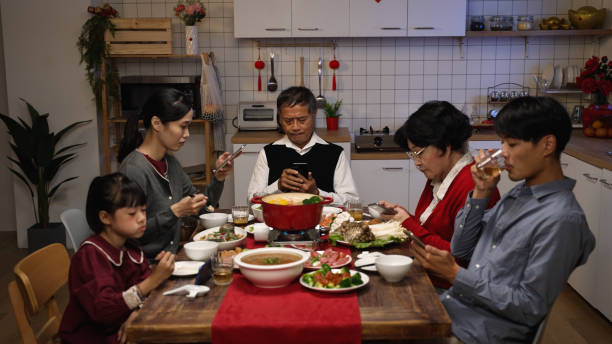 家庭で中国の大晦日のテーブルで再会ディナーをしながら、携帯電話で遊んで、お互いを無視して混合世代を持つアジアの家族 - family room ストックフォトと画像