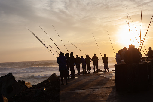 Fishing silhouetted unrecognizable fishermen by the ocean sea river mouth block early morning dawn sunrise recreational lifestyle.