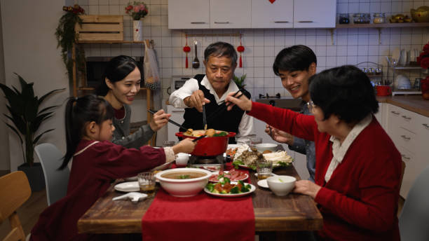 幸せなアジアの拡張家族は、自宅で中国の新年の同窓会の夕食中に一緒に鍋を調理しながら、箸で食材を置きます - family room ストックフォトと画像