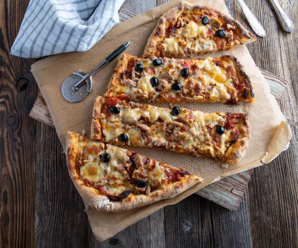 Traditional italian pizza with tuna, onions, mozzarella cheese and tomato sauce served on wooden table with pizza cutter. Closeup and overhead view