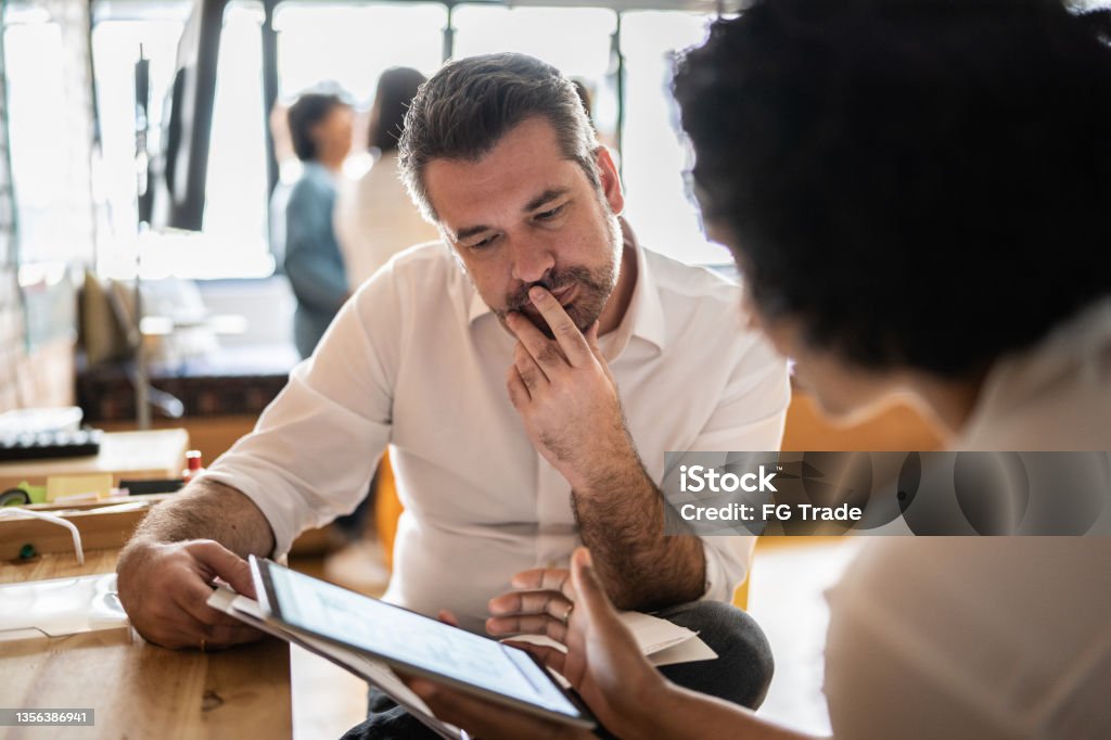 Mature man looking at a digital tablet that a colleague is showing at work Advice Stock Photo