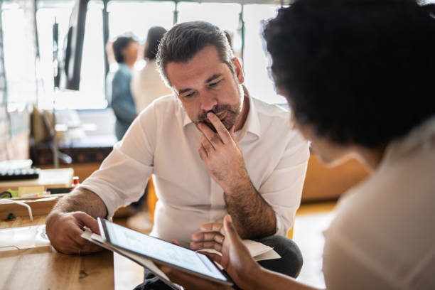 Mature man looking at a digital tablet that a colleague is showing at work Mature man looking at a digital tablet that a colleague is showing at work studying stock pictures, royalty-free photos & images