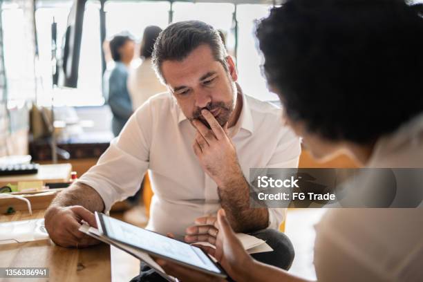 Mature Man Looking At A Digital Tablet That A Colleague Is Showing At Work Stock Photo - Download Image Now
