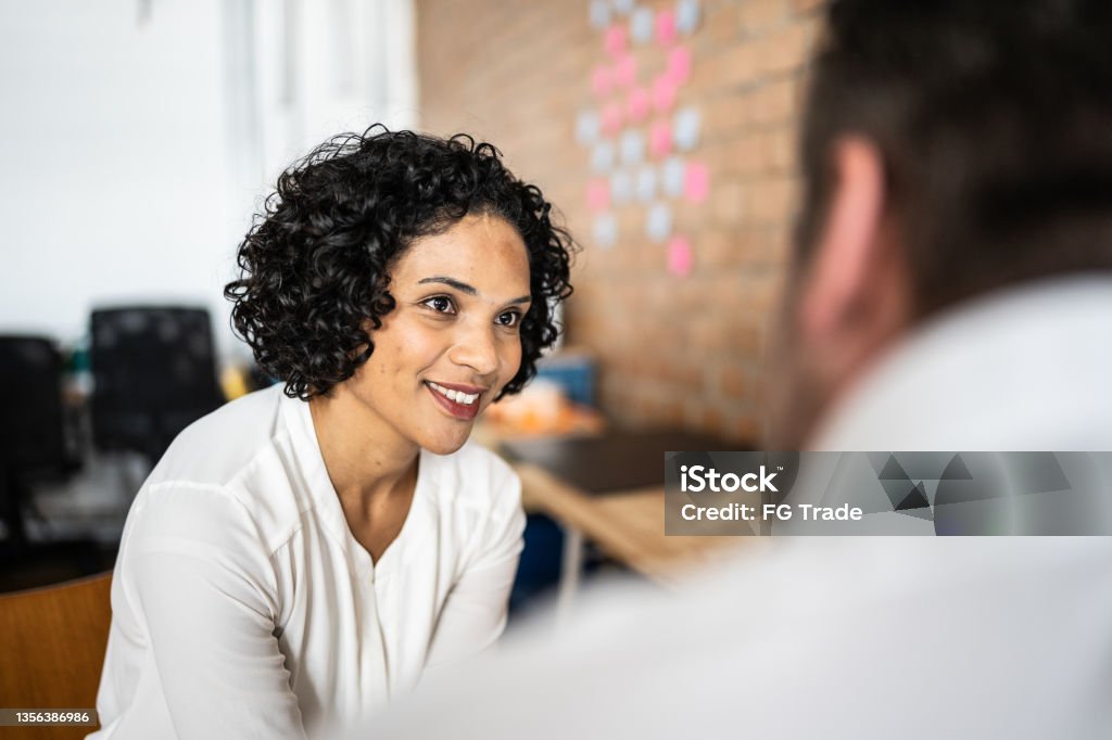 Mid adult woman talking with a colleague at work Feedback Stock Photo