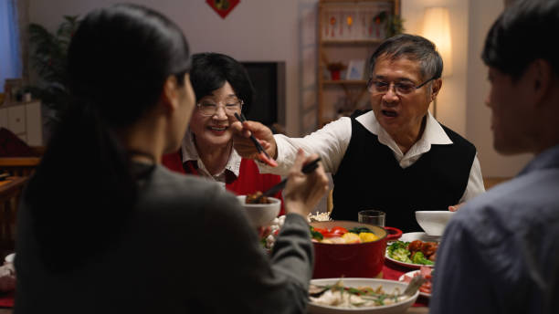 istock selective focus with over shoulder view smiling asian elderly couple grandfather and grandmother holding food with chopsticks and giving to their daughter in law at dinner table on eve of new year 1356387154