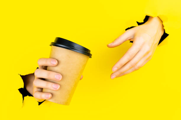 istock Hand is holding paper coffee cup in torn hole 1356389281
