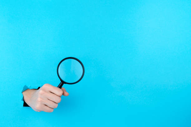 istock Hand is holding black magnifying glass in torn hole 1356389360