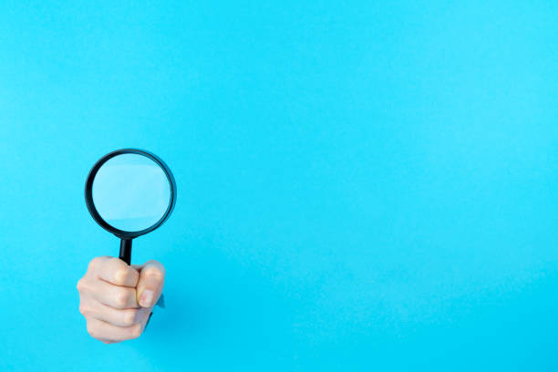istock Hand is holding black magnifying glass in torn hole 1356389542