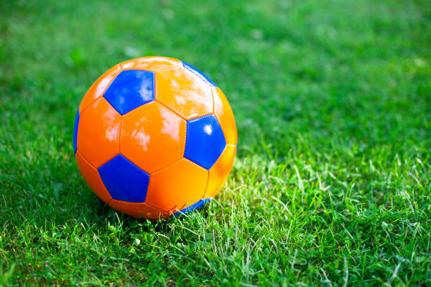 Close up of bright orange and blue football ball on a green grass. stock photo