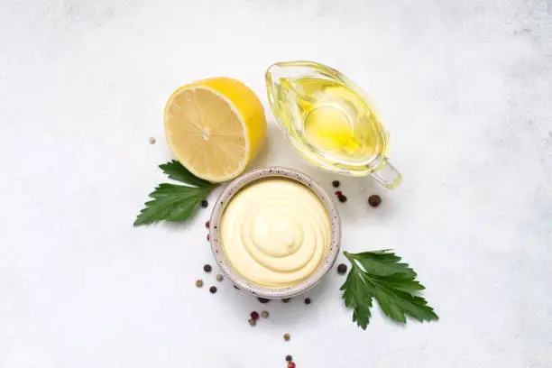 ingredients for mayonnaise: egg, lemon, garlic, mustard on the middle side on grey background.