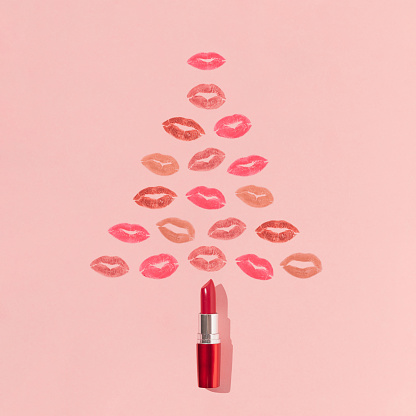 Christmas tree shape made of lipstick and colorful lip prints on bright pink background. Minimal New Year beauty concept. Creative make up or cosmetic aesthetic. Holiday kisses pattern.