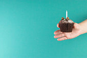Birthday holiday. Chocolate muffin with candles in a female hand. Homemade dessert on a blue background. Copy space.