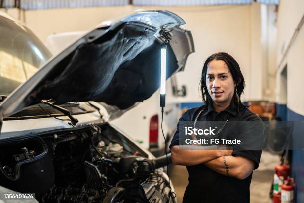 Portrait Of Nonbinary Person Repairing A Car In Auto Repair Shop Stock Photo - Download Image Now