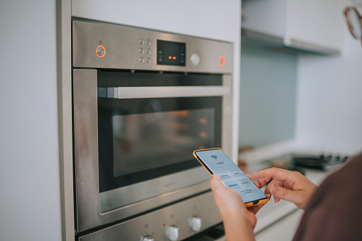 asian chinese Woman heat up food controlling microwave with a smart phone app at home