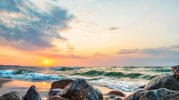 Sunset in the wavy sea with a beautiful multicolored sky with clouds, large rocks in the foreground Sunset in the wavy sea with a beautiful multicolored sky with clouds, large rocks on the sandy shore in the foreground, seascape sunset beach hawaii stock pictures, royalty-free photos & images