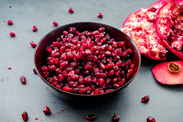 A wooden bowl full of fresh pomegranate arils with a seeded fruit