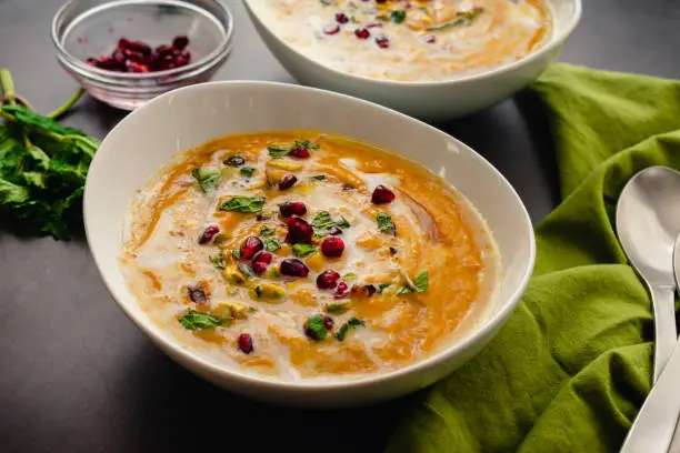 Roasted pumpkin soup garnished with mint leaves, pomegranate seeds, and chopped pistachios