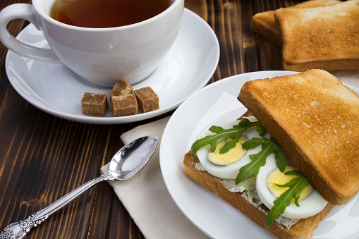 Vegetarian sandwich with eggs, arugula and tea in the white cup. Close-up. Breakfast.