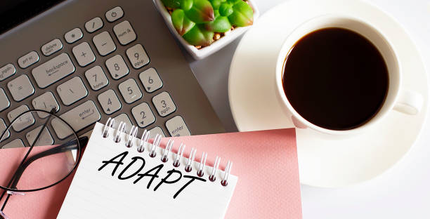 istock Office supplies, devices, coffee cup and glasses on white table with text ADAPT 1356408781