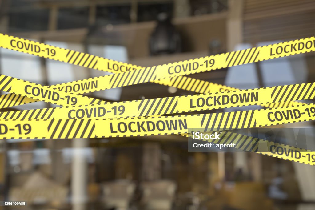 Barrier Tape restricting access to a restaurant or shop. Warning text "COVID-19" and "LOCKDONW" on the tape. Lockdown Stock Photo