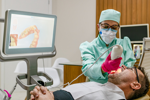 Young dentist woman performing 3d scan of man teeth