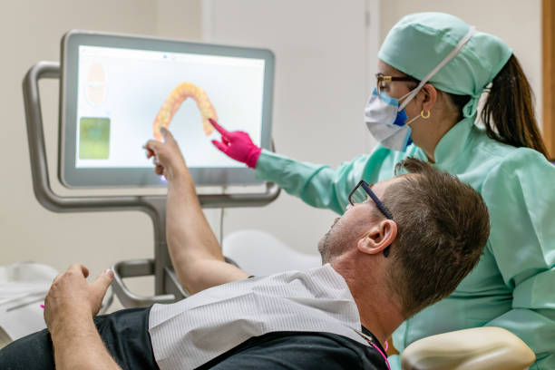 Patient and dentist discussing the need for intervention in the patient's teeth with the 3D technology aid Patient man and young dentist woman discussing the need for dental procedure on the patient's teeth with the help of 3D tooth scanner technology and touch screen 3d scanning photos stock pictures, royalty-free photos & images