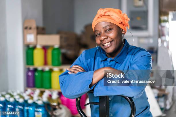 Mid Adult African Woman With Hand Pallet Standing In A Distribution Warehouse Portrait Of A Happy Afro Woman With Headscarf Wearing Uniform Working In A Factory Warehouse Stock Photo - Download Image Now