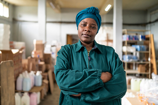 Retrato de una mujer afro segura de sí misma con pañuelo verde en la cabeza y brazos cruzados, vestida con ropa de trabajo en su espacio de trabajo photo