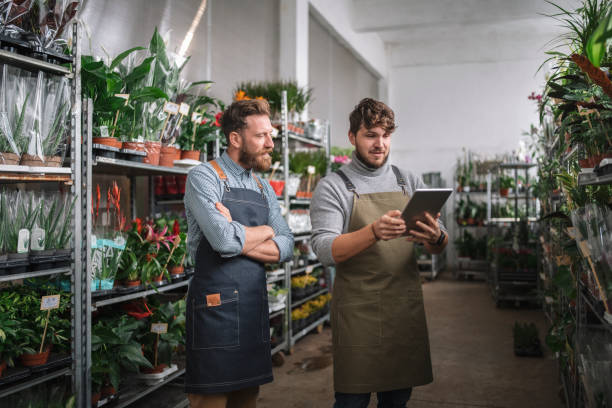 uso de la tecnología en pequeñas empresas, trabajadores masculinos que usan tableta digital en el almacén de flores. - florist small business flower shop owner fotografías e imágenes de stock