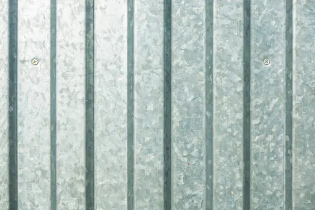 The wall is made of gray profiled metal sheet. A galvanized zinc pattern is visible on the surface. Background. Texture.