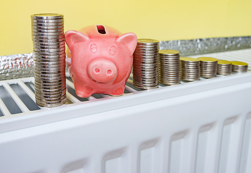 Pink piggy bank with coins on the heating radiator at home.
