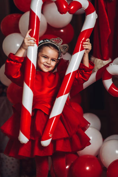 lächelndes weibliches kind mit lieblings-zuckerstangenballons während der weihnachtsfeier - puffed sleeve stock-fotos und bilder