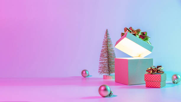 istock Christmas gift box neon background. Open xmas gift box with shine lights, minimal tree. Holiday decoration bauble ball on neon abstract gradient backdrop. Happy new year copy space. 1356420358