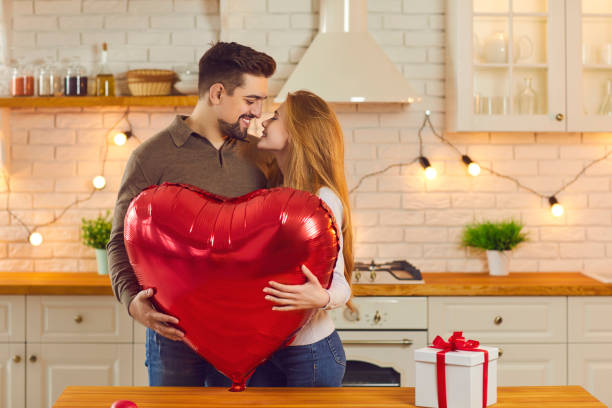 Happy young couple holding huge heart-shaped balloon and kissing on Saint Valentine's Day stock photo